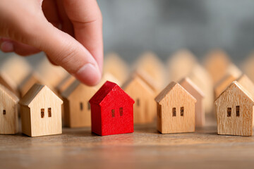Hand placing red house model among many wooden houses home choice real estate selection