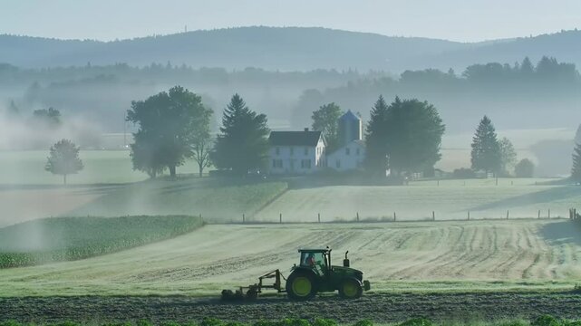 Tranquil morning on a farm with a tractor working the fields amidst misty mountains
