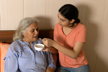 Indian granddaughter taking care of grandmother at home helping her on daily basis serving food.