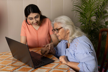 Indian young granddaughter taking care of grandmother at home helping her in learning online...