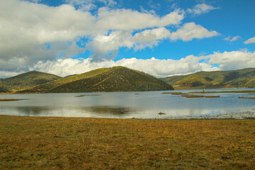 Golden forests surround serene alpine lakes, reflecting clouds Pudacuo National Park, Yunnan, China, Shangri-La, lake
