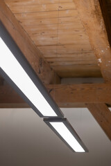 Close-up of suspended linear LED light fixture mounted to exposed wooden beam ceiling