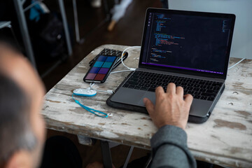 Developer programming on laptop with code editor visible alongside smartphone and charging cables