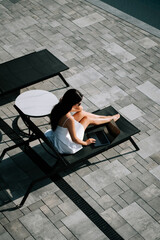 Woman relaxing on a sun lounger by the poolside in bright sunlight during a summer day