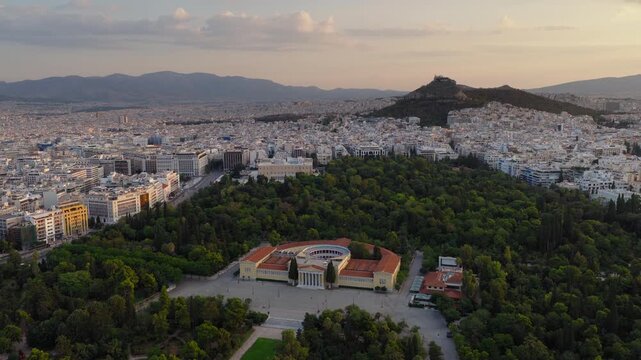 Slow panning drone shot of Zappeion Hall in Athens at sunrise with Lycabettus Hill in the background and clouds glowing in the morning sky