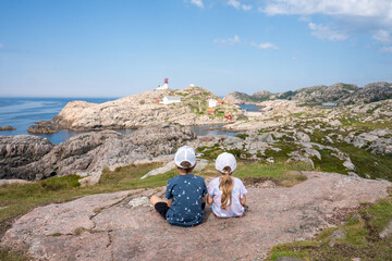 Two small children sitting on a rock looking at the Lindesnes Lighthouse. Lindesnes Fyr on most southern point of Norway, Europe. 