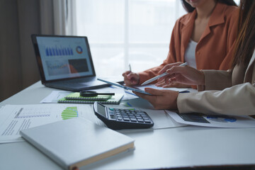 Businesswomen are working together in office, analyzing financial charts and graphs using laptop and tablet, discussing business strategy and planning for future investment