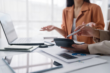 Two businesswomen are using calculator and digital pen to calculate financial data on desk in office, working together to analyze and plan investment strategy