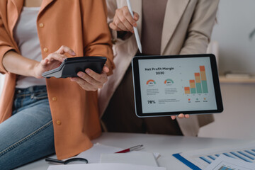 Two businesswomen are working together, calculating and analyzing financial data using calculator...