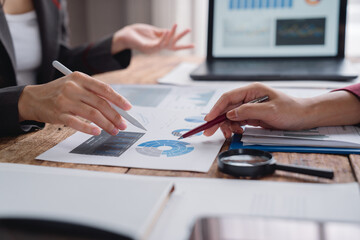 Fototapeta premium Businesswomen are analyzing financial charts and graphs using magnifying glass and pens during a meeting to discuss investment strategy and business performance