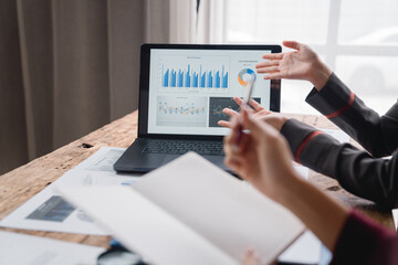 Businesswomen are discussing company performance using charts and graphs displayed on laptop during a meeting, demonstrating collaborative data analysis for strategic decision-making