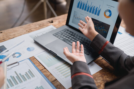 Business professionals engaging in a discussion about company performance, analyzing graphs and charts displayed on a laptop, with various supporting documents organized on the table