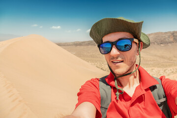 Tourist wearing sunglasses and hat taking a selfie on top of a sand dune in Altyn Emel National Park