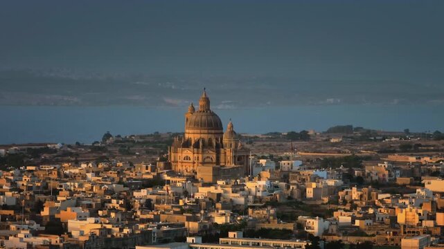 Malta, Comino island: Majestic village of Gharb in Gozo. Malta. Church of Saint John the Baptist, Xewkija or Xewkija Rotunda. City buildings and sea under dramatic evening sky. Drone flight footage