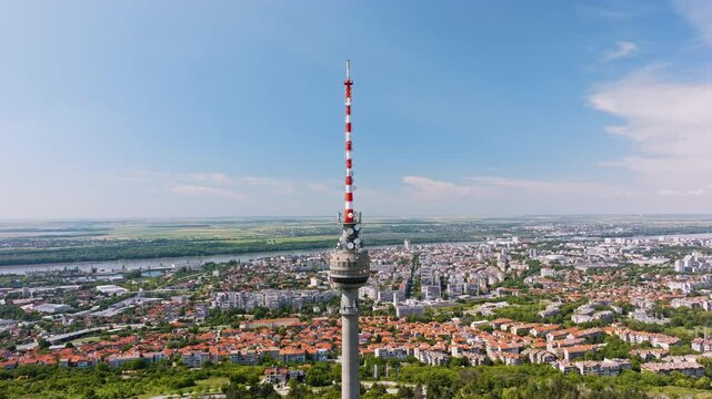 Travel drone shot Ruse Bulgaria high telecommunications tower above green urban forest and city, representing modern broadcasting infrastructure, tourism development, unique Balkan architecture