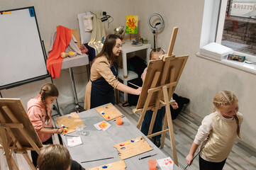 Teacher explains to kids how to draw pictures in art class. School children drawing brush...