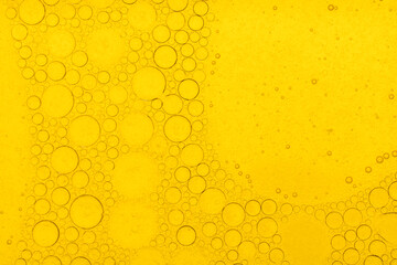 Macro abstract image of golden oil bubbles suspended in liquid, forming overlapping circular patterns. The texture and light create a warm, artistic background perfect for cosmetic, beauty