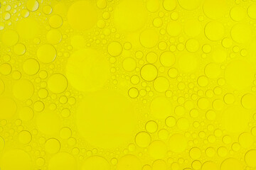 Macro abstract image of golden oil bubbles suspended in liquid, forming overlapping circular patterns. The texture and light create a warm, artistic background perfect for cosmetic, beauty