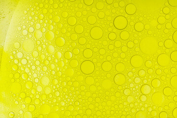 Macro abstract image of golden oil bubbles suspended in liquid, forming overlapping circular patterns. The texture and light create a warm, artistic background perfect for cosmetic, beauty