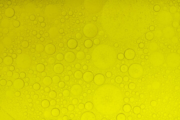 Macro abstract image of golden oil bubbles suspended in liquid, forming overlapping circular patterns. The texture and light create a warm, artistic background perfect for cosmetic, beauty