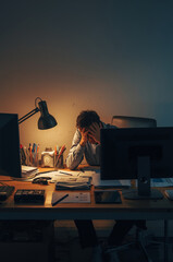 Stressed office worker at messy desk between monitors at night, burnout concept