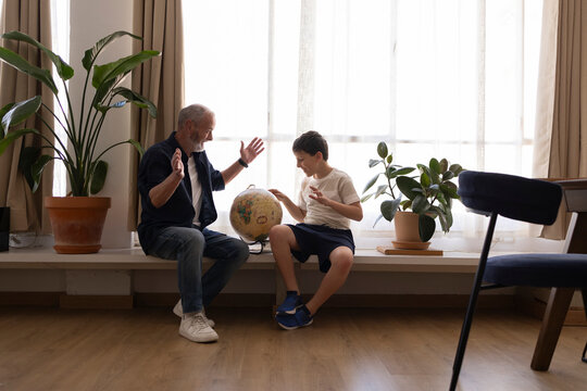 Grandfather and grandson exploring geography together with globe indoors