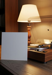 A blank, gray vinyl album cover leans against a vintage record player under the warm, ambient light of a classic desk lamp.