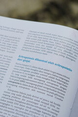A close-up of an open medical textbook, showing detailed text and diagrams about human physiology...