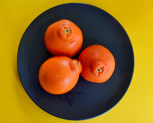 Three juicy tangelos on a black plate.
