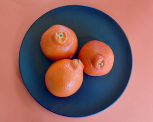 Three juicy tangelos on a black plate.