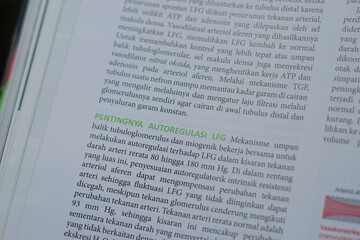 Naklejka premium A close-up of an open medical textbook, showing detailed text and diagrams about human physiology and biology. This image represents study, education, research, and the journey of a medical student.