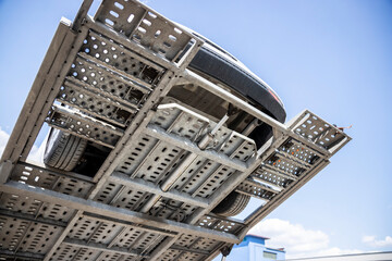 Visible chassis and bottom of pre-owned car on upper car hauler platform, white wagon on car...