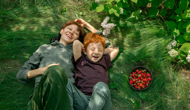 Mother and son with red hair laughing together on grass with berries