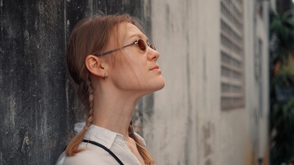 Obraz premium Woman with braids enjoys a moment of reflection by a weathered wall in an urban setting