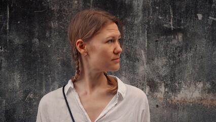 Woman with braided hair stands confidently against a textured wall in a casual outfit while...