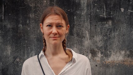 Portrait of a woman with braids standing against a textured gray wall in urban setting during...