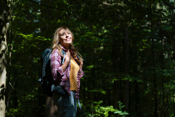 Smiling hiker with backpack enjoying sunlight in forest