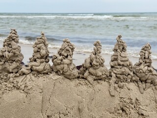 Unique drip sandcastle sculptures lined up on a beach with ocean waves in the background. Creative...