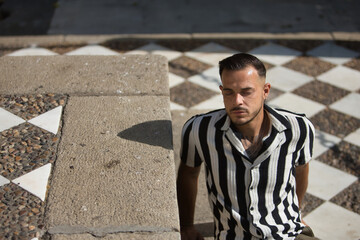 Young, brunette, Hispanic, modern man in crochet shirt with black and white stripes and jeans, eyes...