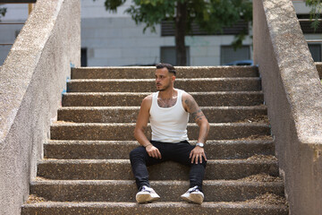 Young, brunette, Hispanic, modern man in white tank top and jeans, with a serious and distracted...