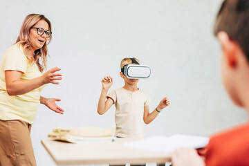 Teacher guiding schoolboy using virtual reality headset in classroom