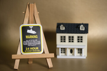 Surveillance warning sign on easel beside model house, highlighting security, monitoring, and crime prevention in a domestic setting.