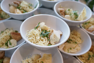A bowl of beef meatballs containing noodles, vermicelli, fried onions and celery leaves.