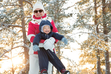 Healthy grandmother spins toddler in snowy forest, golden winter light, joyful family moment,...