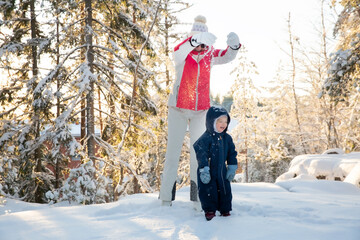 Healthy grandmother and toddler play in snowy forest, tossing snow, enjoying golden winter light,...