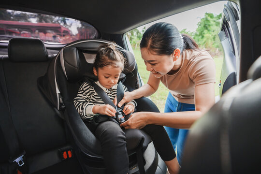 mother is fastening safety belt to toddler girl in car seat, safety baby chair travelling