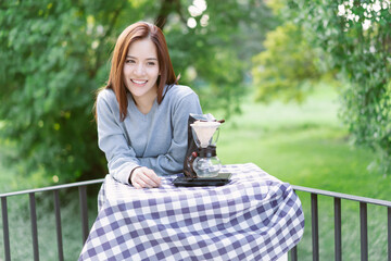 Cheerful Asian woman enjoying morning outdoors with coffee brewing equipment on table. Lifestyle...