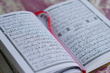 A close-up of an open Al-Quran, the holy book of Islam, showing its beautiful Arabic script and calligraphy. This image represents prayer, worship, study, and spiritual devotion, especially during Ram