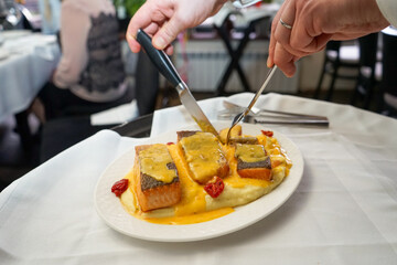 The waiter is cutting the fish on the plate.
