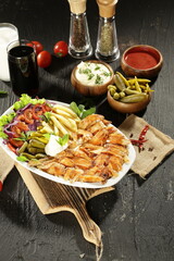 Traditional Turkish Doner Kebab Plate with Fresh Vegetables, French Fries, and Sauces on Rustic Background